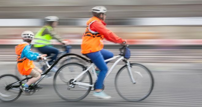 Young family with a child ride a bikes on a city streets. Intentional motion blur and color shift
