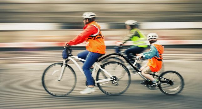 Young family with a child ride a bikes on a city streets. Intentional motion blur and color shift