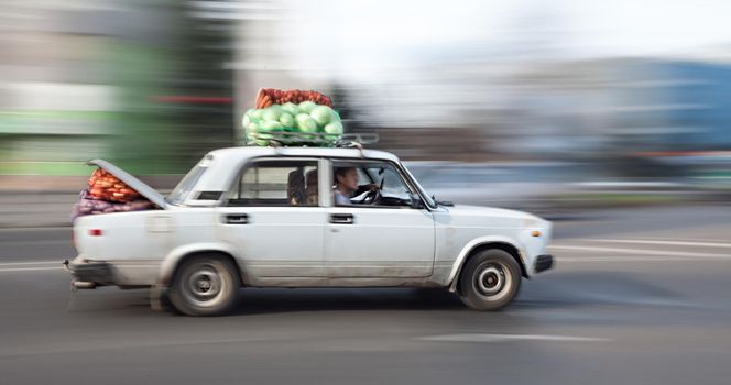 Old car loaded with cabbage and carrots rides through the city streets. Intentional motion blur