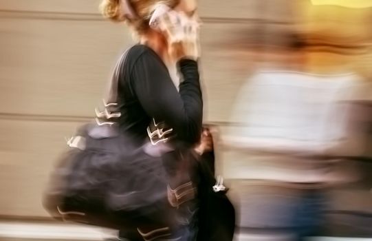 Hot day in the city. Woman talking on a cell phone in a hurry. Intentional motion blur and color shift