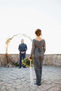 A bride with a bouquet in her hand goes to the groom who is waiting for her at the wedding arch . High quality photo