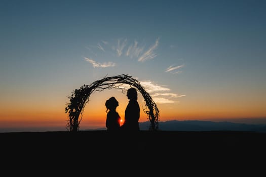 Silhouettes of bride and groom holding hands near the wedding arch at sunset at the wedding ceremony. High quality photo