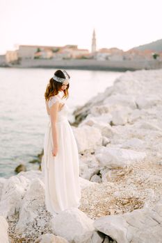 A sophisticated bride stands on a picturesque rocky shore near the old town of Budva . High quality photo