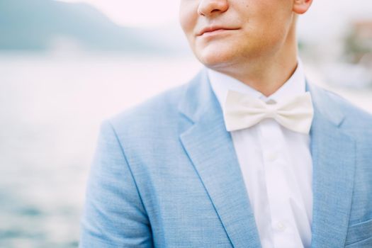 A man in a blue jacket and a white bow tie stands by the sea, close-up . High quality photo