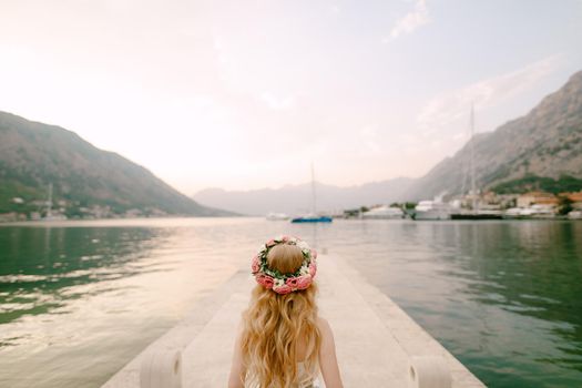 A bride in a delicate wreath of roses stands on a pier near Kotor in the Bay of Kotor, back view . High quality photo