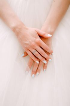 Graceful hands of the bride folded on a fluffy skirt of a wedding dress, close-up . High quality photo
