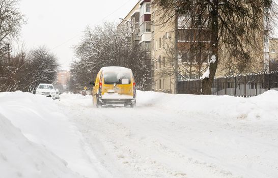 Lutsk, Ukraine - February 12,2020: Stuck car in snow and ice. City street after blizzard. Buried vehicle in snowdrift. Parking in winter after snowfall. Uncleaned road. Record-breaking amounts of snow