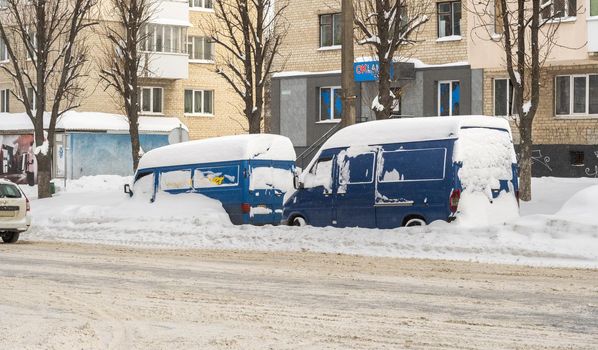 Lutsk, Ukraine - February 12,2020: Stuck car in snow and ice. City street after blizzard. Buried vehicle in snowdrift. Parking in winter after snowfall. Uncleaned road. Record-breaking amounts of snow