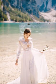 A beautiful bride in a white chiffon dress with sleeves and lace on the shores of Lake Lago di Braies in Italy. Destination wedding in Europe, on the popular Braies lake.