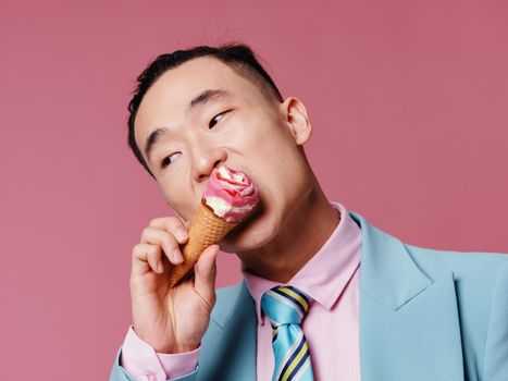 Asian man in a suit eating ice cream in a cone on a pink background business finance. High quality photo