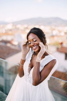 A beautiful African-American bride in white wedding dress, touches her face in vintage gloves. Fine-Art wedding in Florence, Italy