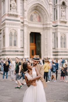 Wedding in Florence, Italy. Caucasian groom hugs from behind African-American bride at Piazza del Duomo. Interracial wedding couple