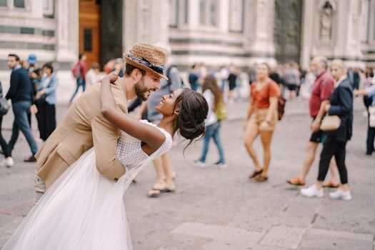African-American bride and Caucasian groom cuddling in Piazza del Duomo. Wedding in Florence, Italy. Interracial wedding couple