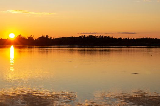 Colorful sunny sunset on a calm lake. The sun is reflected on the surface of the water.