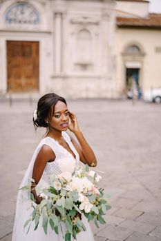 African-American bride in white dress and long veil. With a lush bouquet of the bride in her hands. Wedding in Florence, Italy.