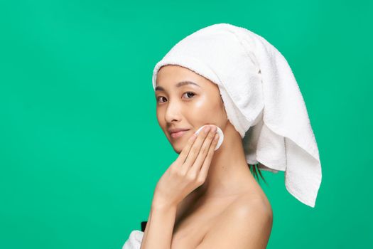 woman with bare shoulders wipes her face but with a cotton pad after make-up Green background. High quality photo