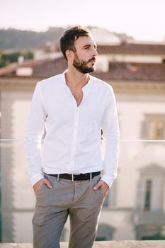 Stylish bearded guy in white shirt and light trousers on a rooftop terrace in Florence, Italy