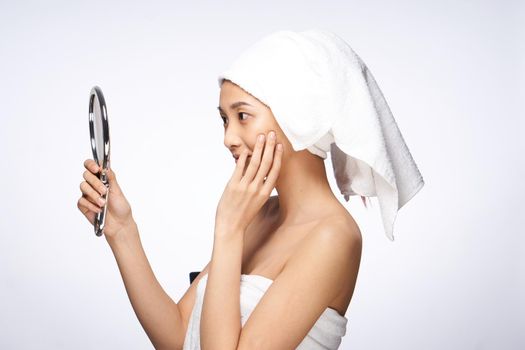 woman of asian appearance after shower looks in the mirror skin care light background. High quality photo