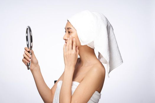 woman of asian appearance after shower looks in the mirror skin care light background. High quality photo