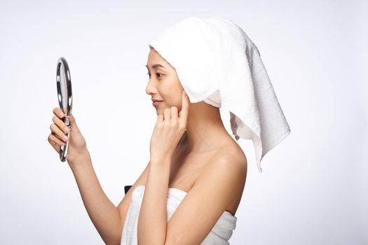 woman of asian appearance after shower looks in the mirror skin care light background. High quality photo