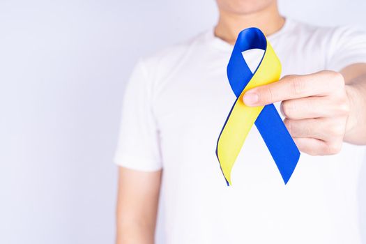 Down syndrome day, hands holding blue yellow ribbon awareness on chest support patient with illness disability