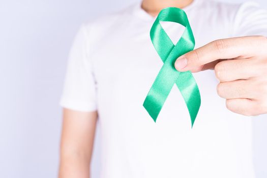 World kidney day, hands holding green ribbon awareness of kidney disease on chest isolated grey background.