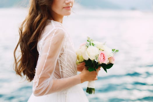 The bride holds a bouquet of roses in her hands and stands on the pier in the Bay of Kotor, close-up. High quality photo