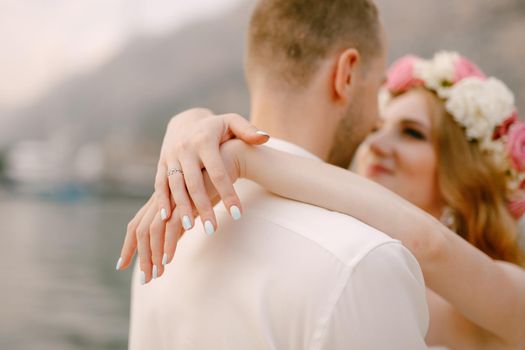 The bride and groom hug on the pier, the bride in a delicate wreath wrapped her arms around the groom's neck. High quality photo