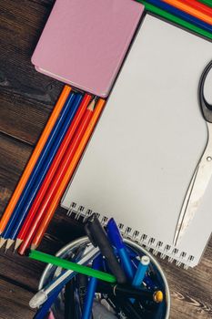 notepads colored pencils and stationery in a glass on a wooden table top view. High quality photo