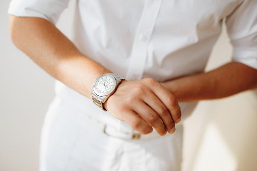 A man in a white shirt puts a watch on his hand during preparation for the wedding ceremony. High quality photo