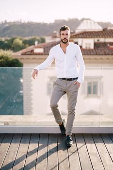 Stylish bearded guy in white shirt and light trousers on a rooftop terrace in Florence, Italy