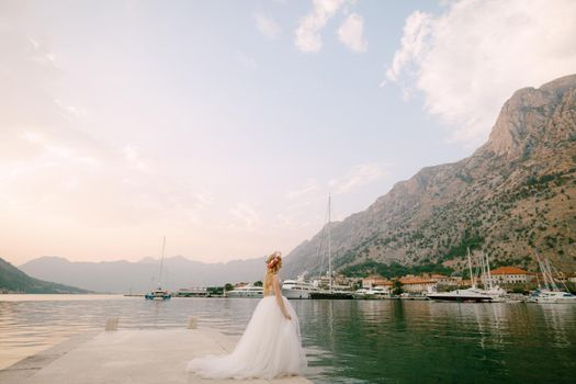 A bride in a delicate wreath of roses stands on a pier near Kotor in the Bay of Kotor. High quality photo