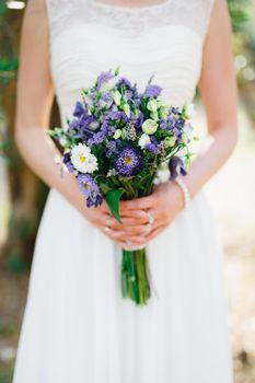 Gentle bride holding a wedding bouquet with blue and white asters, lisiantuses and lavender in her hands, close-up . High quality photo