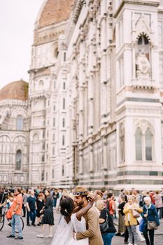 African-American bride and Caucasian groom kissing among the crowd in Piazza del Duomo. Wedding in Florence, Italy. Mixed-race wedding couple