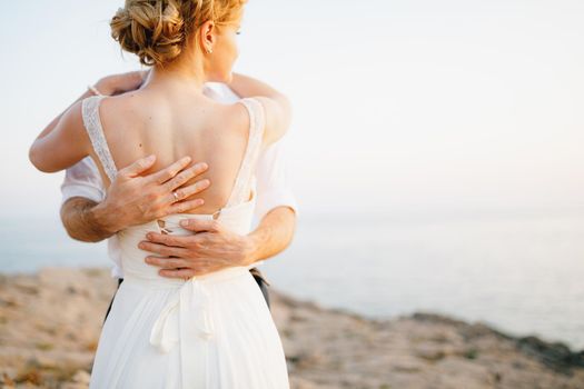 The bride and groom hug on the rocks by the sea against the backdrop of the mountains and the island of Mamula, back view. High quality photo