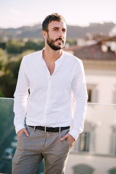 Stylish bearded guy in white shirt and light trousers on a rooftop terrace in Florence, Italy