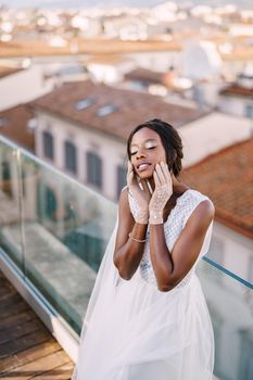 A beautiful African-American bride in white wedding dress, touches her face in vintage gloves. Fine-Art wedding in Florence, Italy