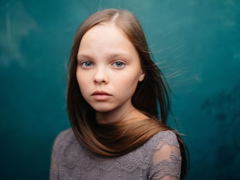 Beautiful little girl in a gray dress close-up cropped view blond hair turquoise background. High quality photo