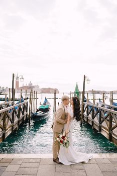 The groom and stand next to the pier for gondolas, hugging, in Venice, near the Piazza San Marco, overlooking San Giorgio Maggiore and the sunset sky. The largest pier for gondolas in Venice, Italy.