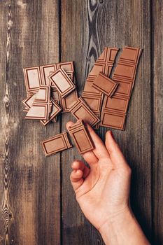 female hand lays out broken chocolate cubes on wooden table. High quality photo