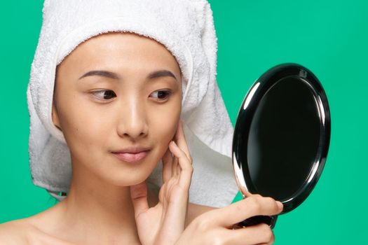 pretty smiling woman with a mirror in her hands a towel on her head skin care green background. High quality photo