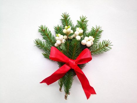 Spruce green branch with white berries with a red ribbon on a white background.