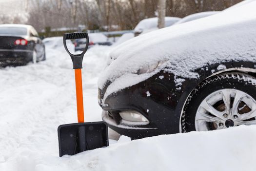 plastic snow shovel in front of snow-covered car at sunny winter morning, close-up with selective focus