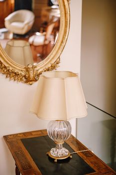 Vintage vintage table lamp with white lampshade and crystal base. An old mirror in a golden frame.