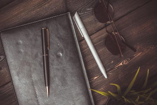 book with black cover and lies on a wooden table and a pen pencil jobs glasses flower potted coffee cup. High quality photo