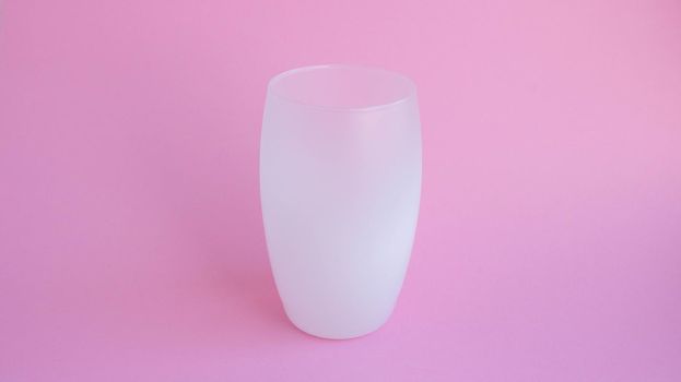 A white frosted drink glass stands on a pink background.