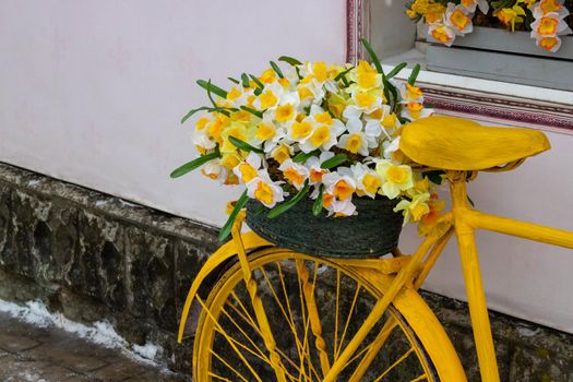 A yellow bicycle wheel with a basket of flowers stands against the wall, in a vintage style.