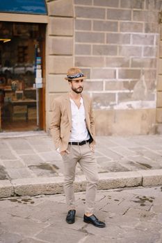 A young guy with a straw hat, a white unbuttoned shirt and a sand jacket, a small beard walks around of Florence.