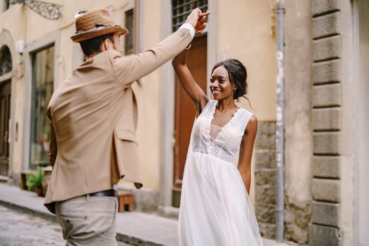 African-American bride and Caucasian groom are dancing on the street. Interracial wedding couple. Wedding in Florence, Italy.