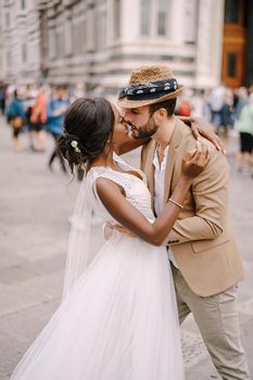 African-American bride and Caucasian groom kissing among the crowd in Piazza del Duomo. Wedding in Florence, Italy. Mixed-race wedding couple